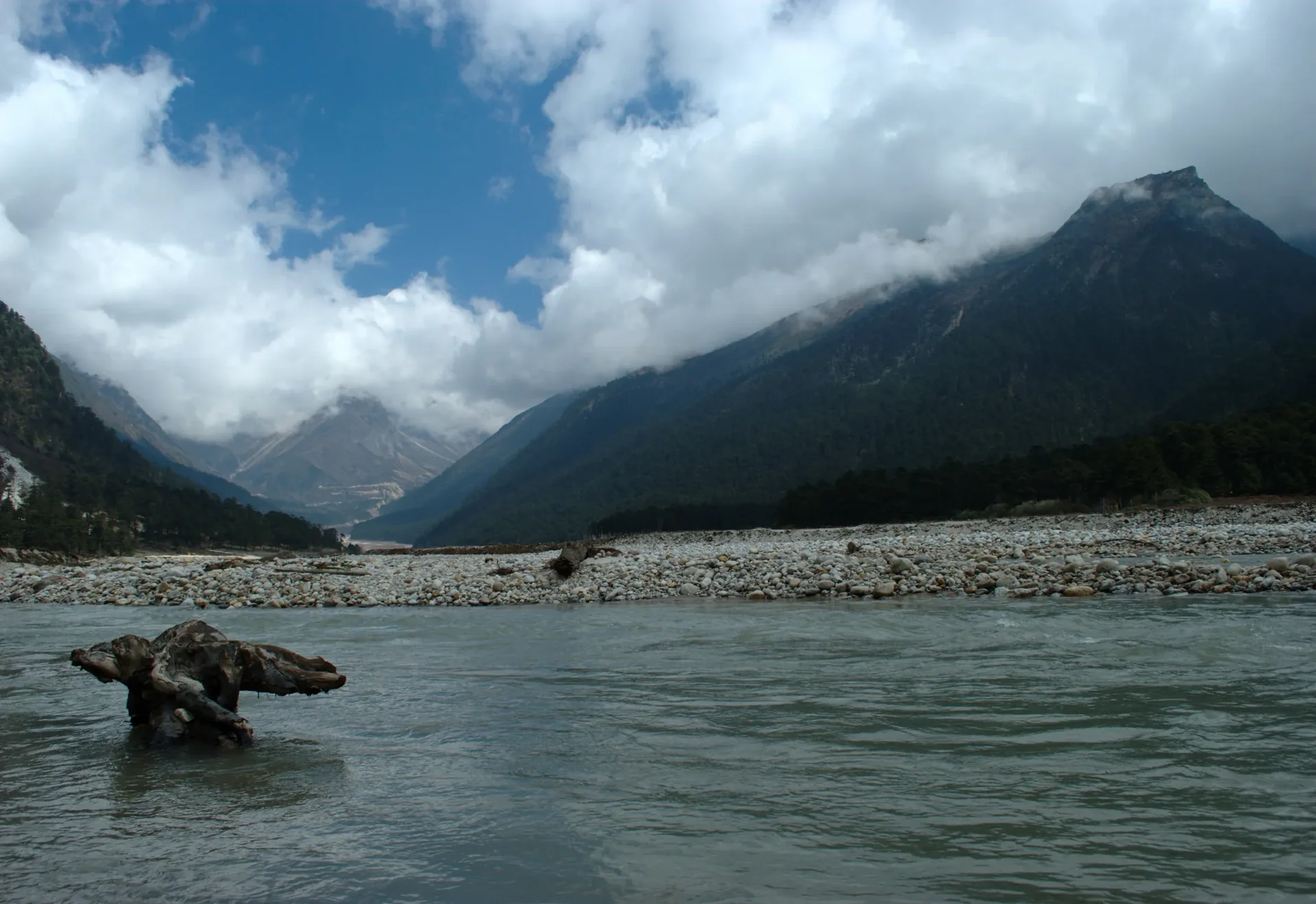 Green mountains and river valley beneath clouds in Sikkim, India.