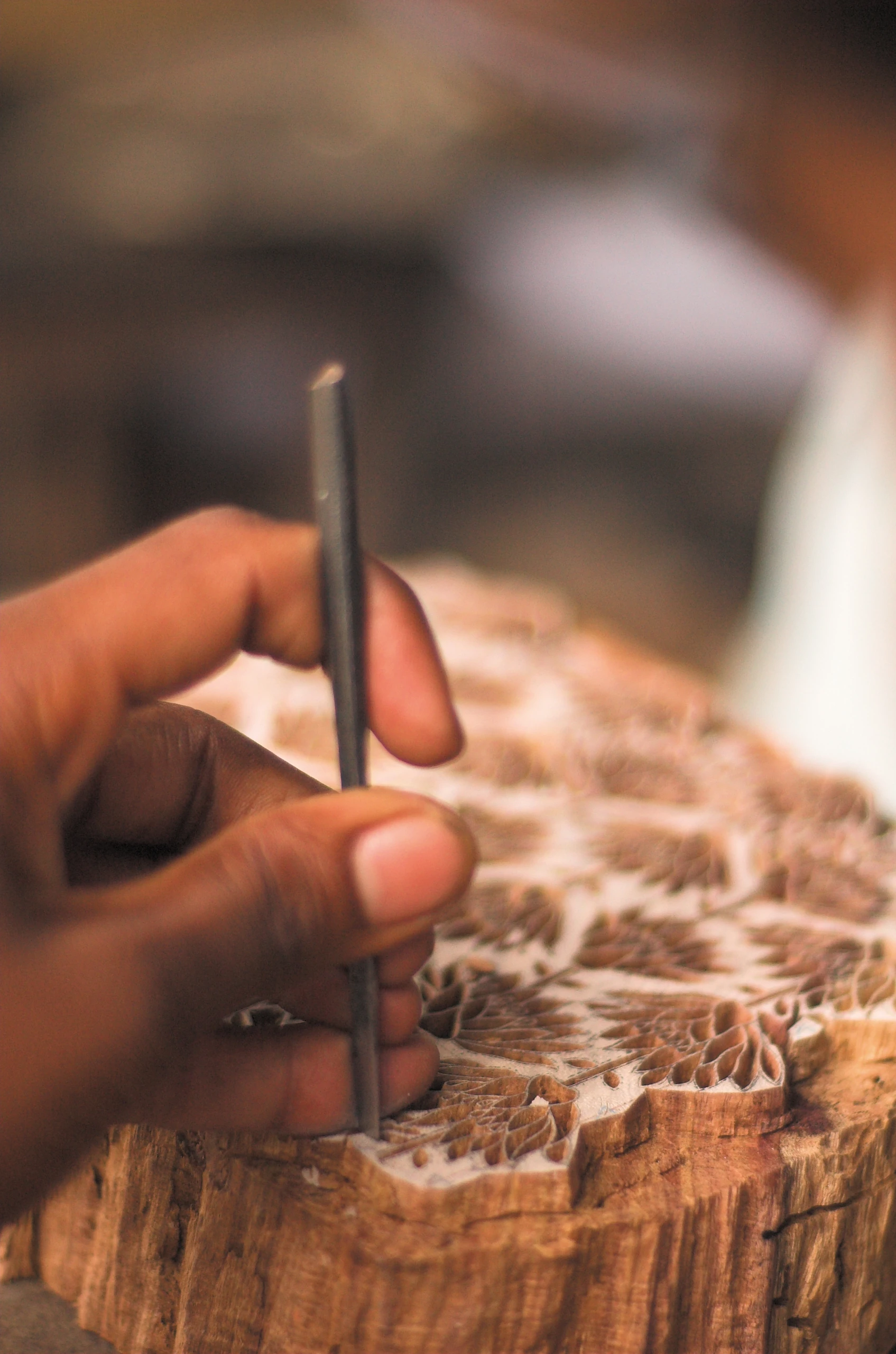 A close view of hands carving an intricate pattern into a wooden printing block