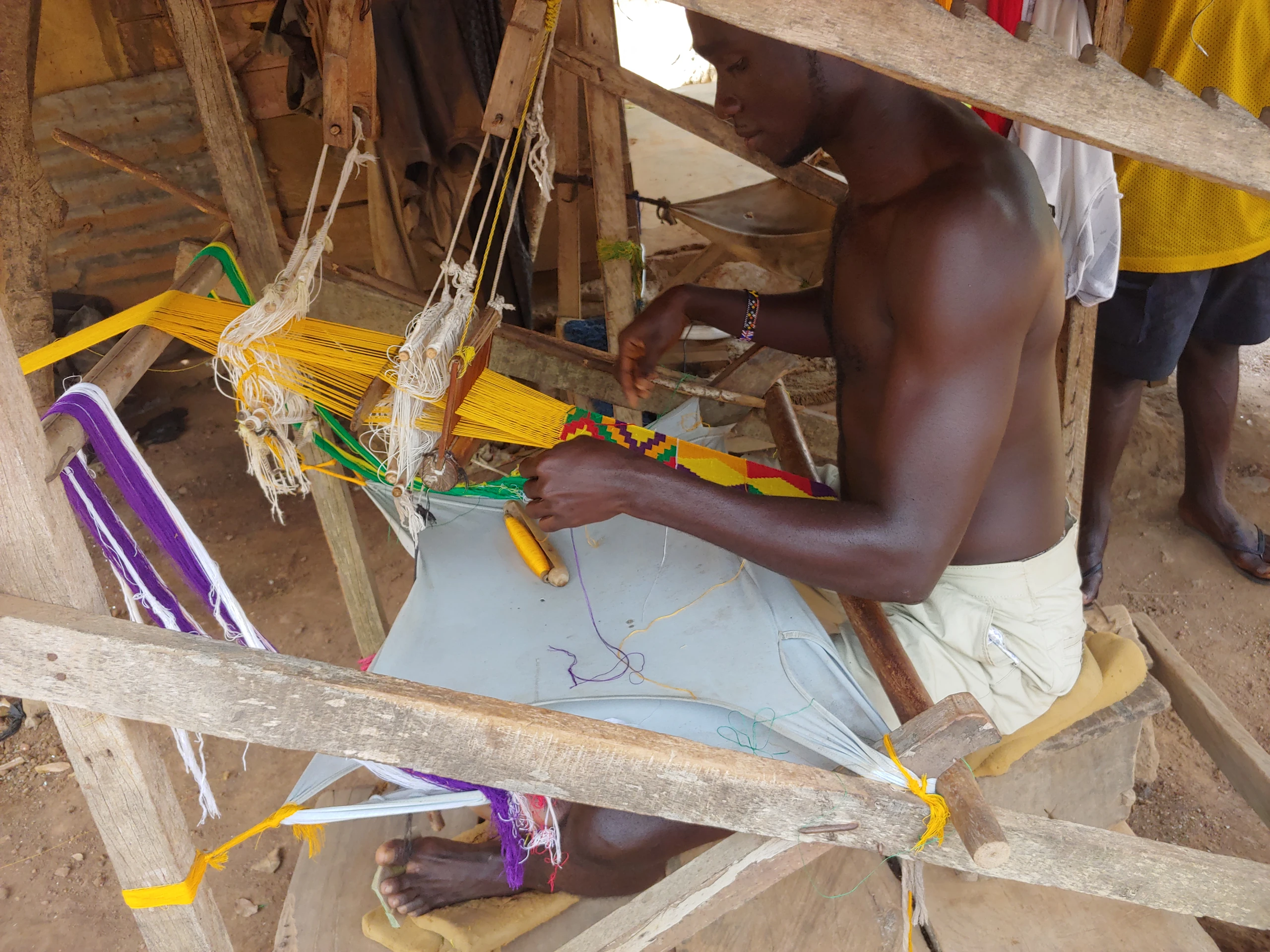 A man guides colourful threads through a traditional Kente loom in Bonwire, Ghana