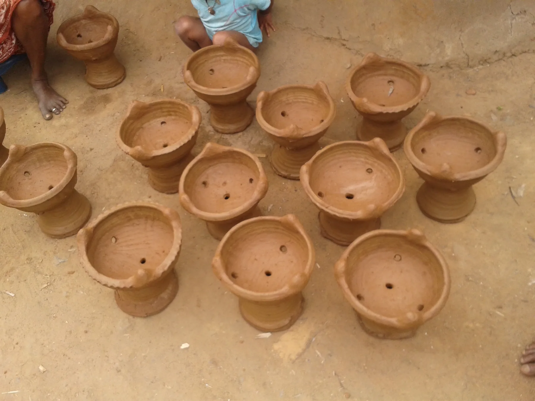 Rows of unglazed earthenware vessels with ventilation holes on the ground at Tantadi Village, India.