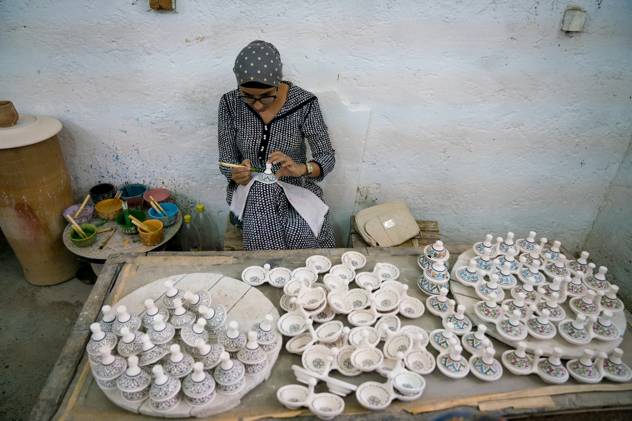 Techniques A ceramic craftswoman in Fez paints a small vessel among rows of unfinished white ceramics