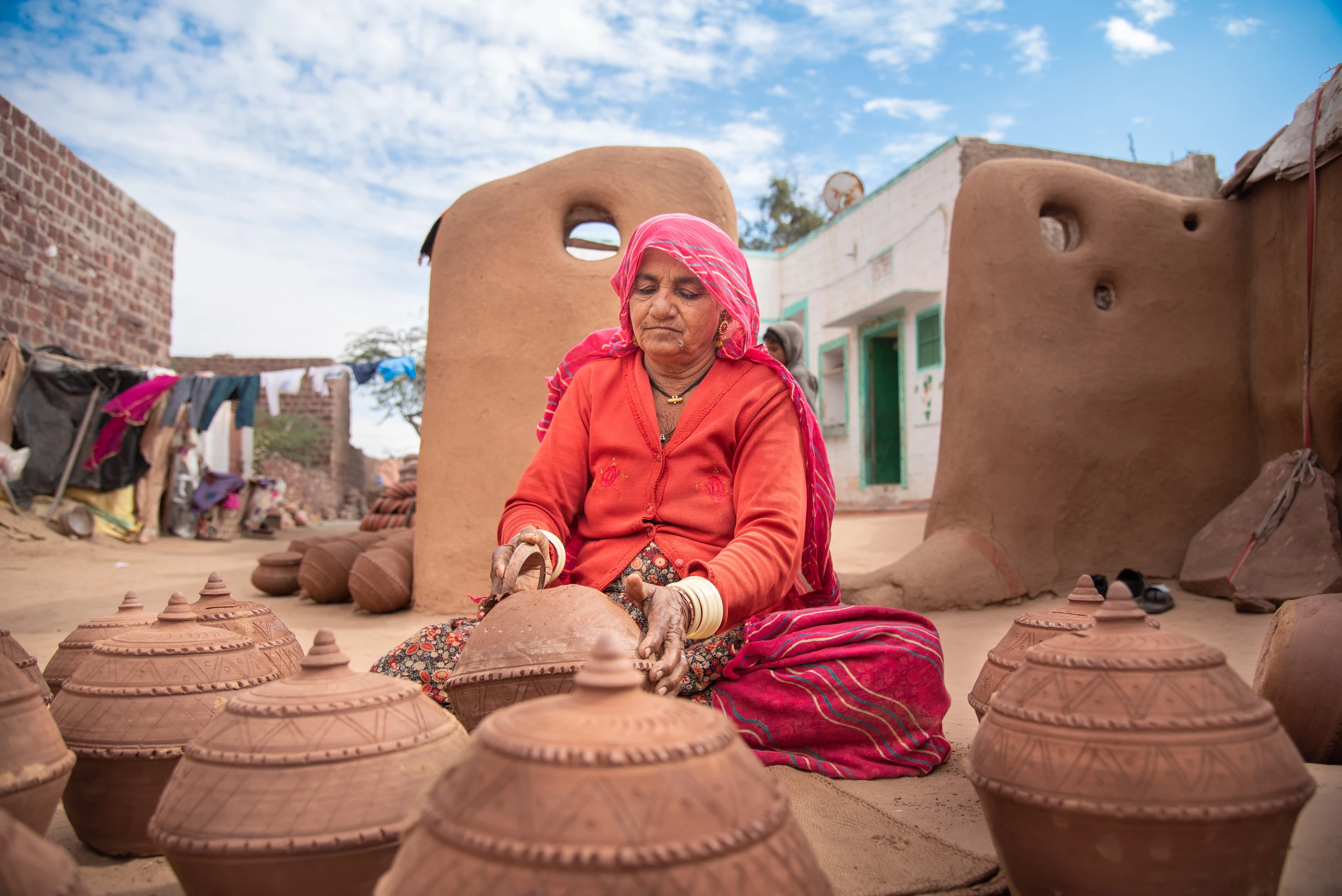 Techniques A woman in red shapes a clay vessel among large earthen pots in Pokaran, Rajasthan